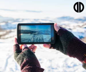Woman taking a photo of a snowing mountain on her phone during winter