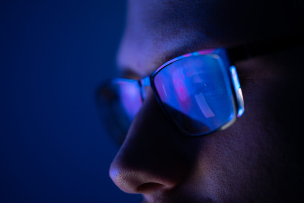 Close-up of a part of a male human face with eyeglasses in neon glow on a background of the vibrant colored liquid