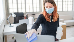 Woman in the office using disinfectant  for sanitizing monitor surface during COVID-19 pandemic