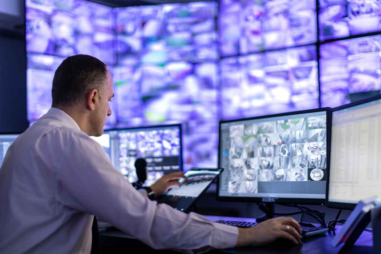 Mature adult man working in surveillance, security and guarding agency and looking at many monitors in front of him; benefits of monitor leasing