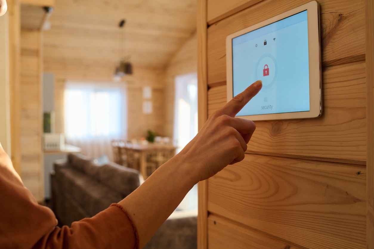 Hand of young woman pointing at screen of alarm system panel with lock sign hanging on wooden wall in living room; The Science Behind Touch Screens