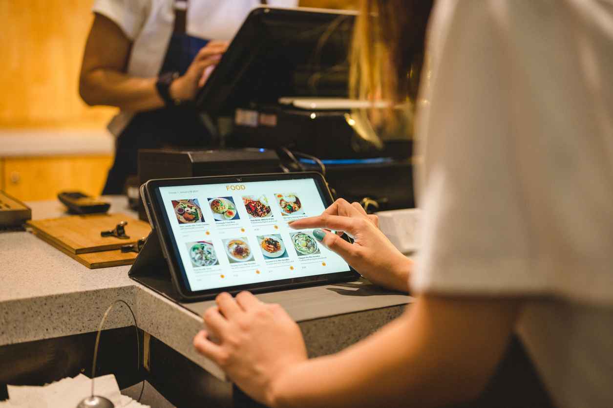 Close-up of hand young Asian woman use digital tablet to buying food on digital tablet at cashier counter; Optical Bonding Solutions for Restaurant Touch Screens