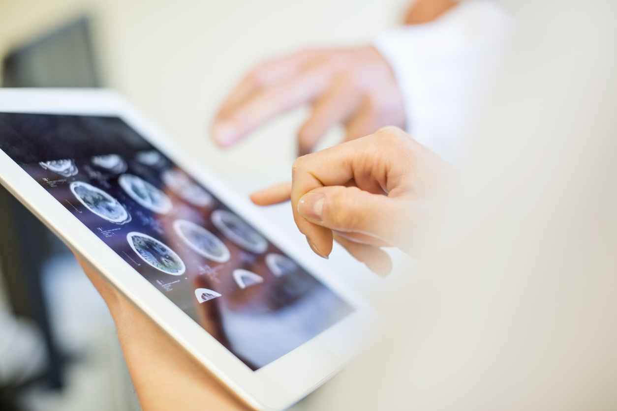 Close up of doctors hands pointing at brain xrays images on digital tablet. Medical team in clinic analyzing MRI scans on digital tablet; Optical Bonding for Medical Devices